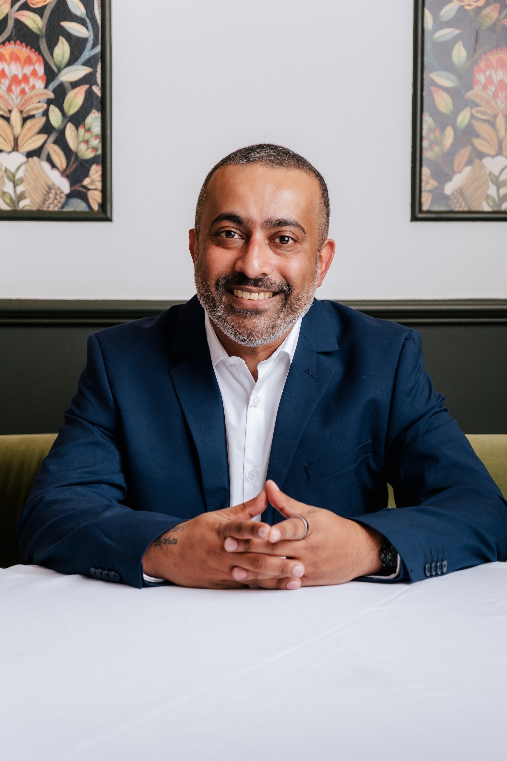 Dr Anith Chacko seated at a table, hands folded, smiling